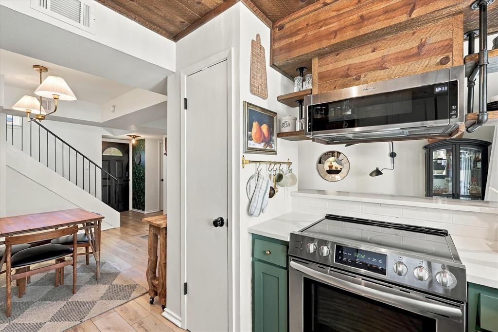 Kitchen featuring green cabinetry, stainless steel appliances, wood-paneled ceiling, and open shelving with industrial pipe detailing