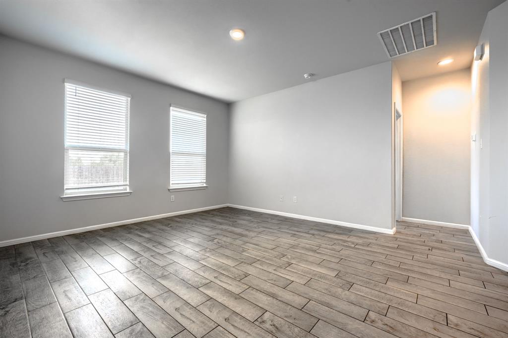 Neutral interior space featuring wood-finish flooring, two windows with integrated blinds, and recessed lighting