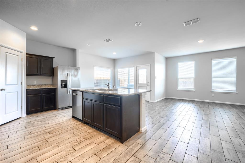 Kitchen featuring dark cabinetry, stone-finish countertops, stainless steel appliances, a center island with a built-in dishwasher, and wood-finish tile flooring