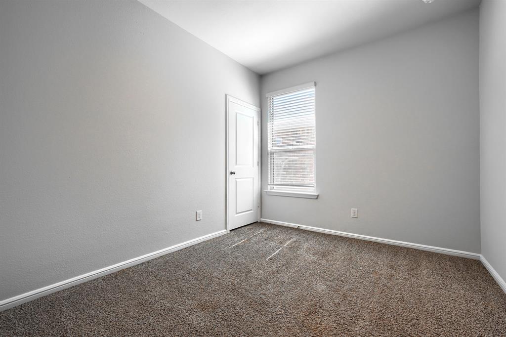 Neutral-toned interior room featuring textured carpeting, a single-panel window with horizontal blinds, and a solid-core interior door