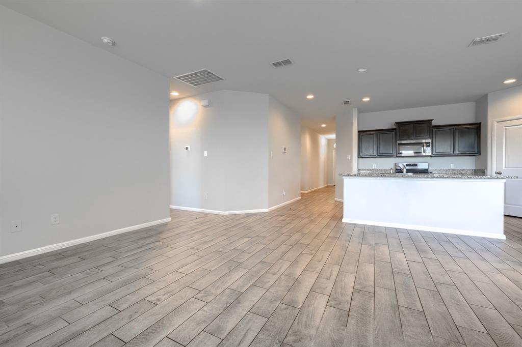 Open-concept interior featuring wood-finish flooring, recessed lighting, a kitchen island with stone-finish countertops, and dark wood cabinetry
