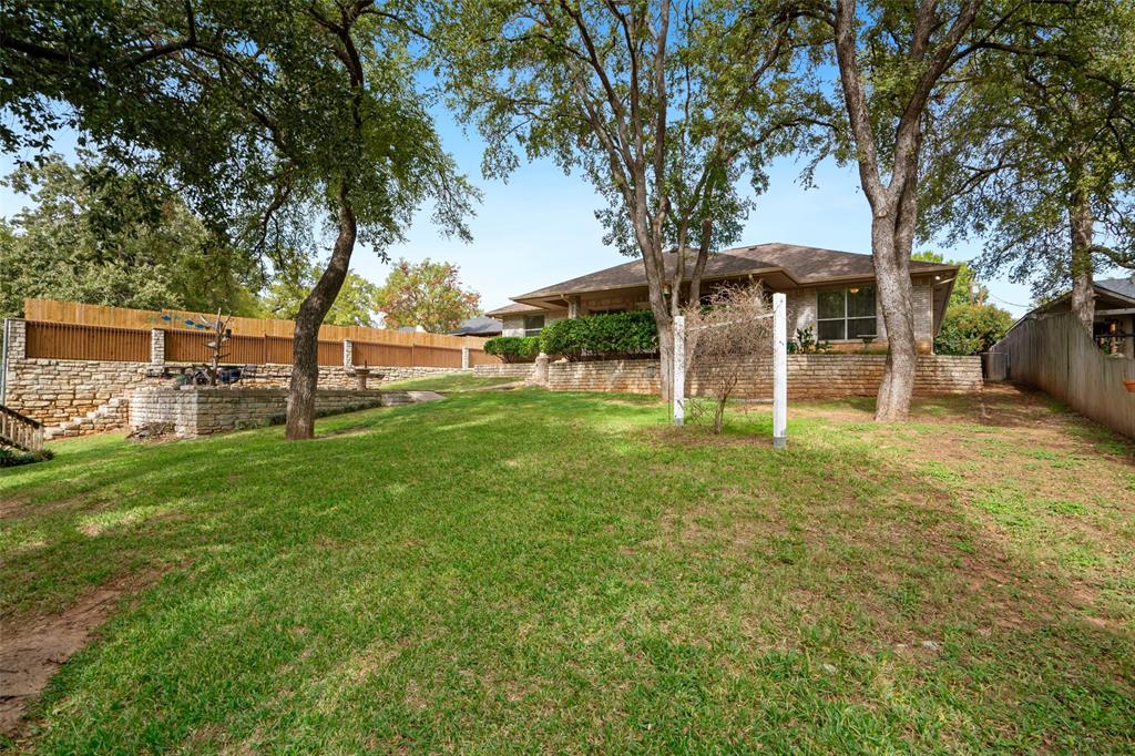 Backyard featuring a tiered stone retaining wall, mature trees, and a manicured lawn