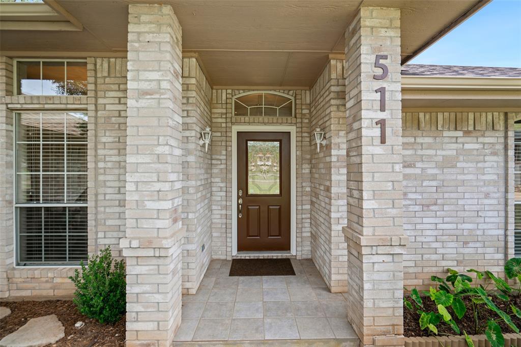 Covered entryway featuring light brick columns, a decorative arch-top transom window, tile flooring, and wall-mounted carriage lights