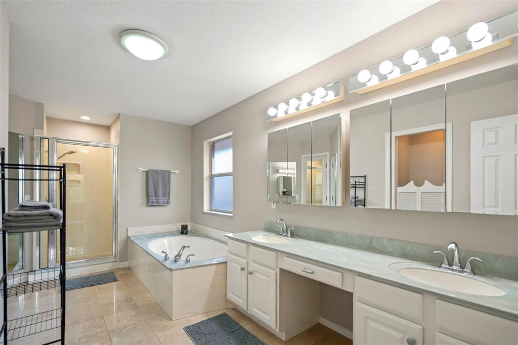 Dual-sinks vanity with countertop seating, garden tub, walk-in glass-enclosed shower, triple-panel mirrored medicine cabinet, tile flooring