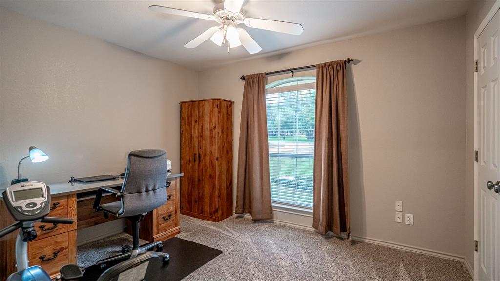 3rd bedroom being utilized at office featuring a central ceiling fan with an integrated light fixture, carpeted flooring, and an arched window
