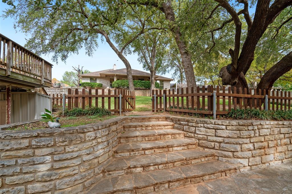 Tiered stone retaining walls, natural flagstone stairs, wood-slat fencing, and mature canopy trees