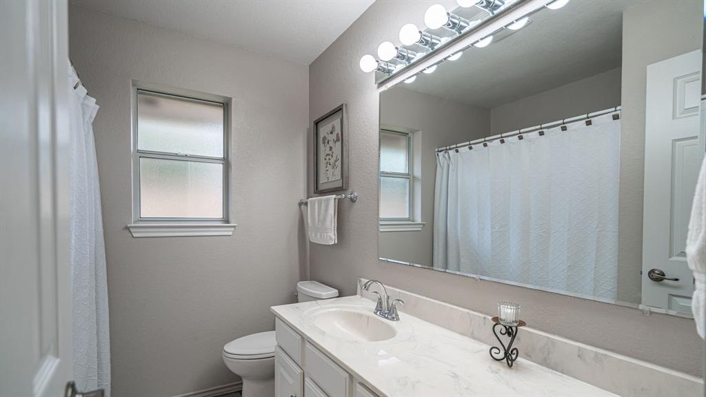 Bathroom featuring a vanity with solid surface countertop and sink, a vanity mirror, integrated multi-bulb vanity lighting, and a window with frosted glass