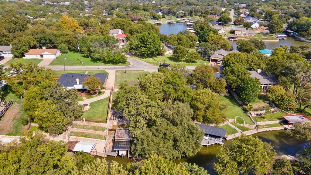 Aerial perspective of a waterfront property featuring a multi-tiered stone retaining wall, private boat slip, mature trees, and direct access to the waterway