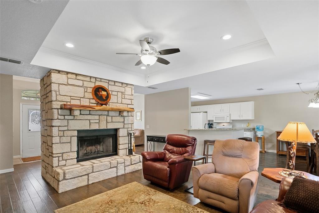 Living area featuring a floor-to-ceiling natural stone fireplace, a natural wood mantel, wood-finish flooring, a tray ceiling, and recessed lighting