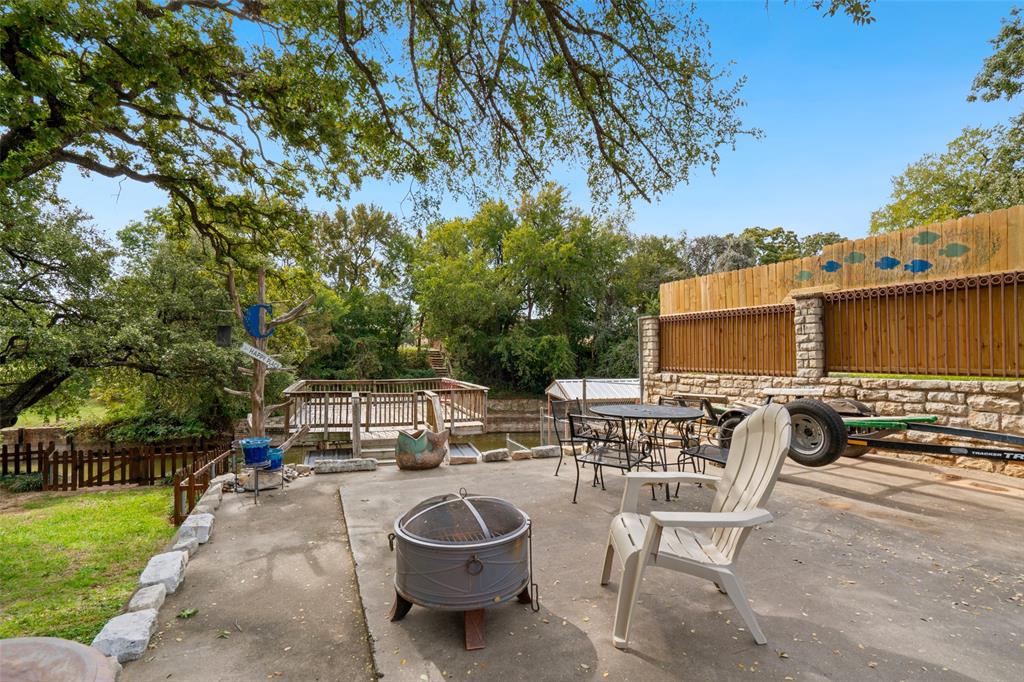 Concrete patio featuring a stacked stone and wooden perimeter fencing, and a wooden deck overlooking lake Granbury accented by mature shade trees