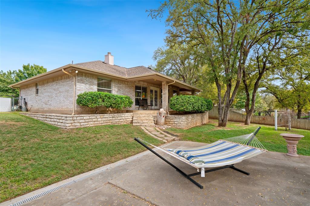 Exterior brick façade featuring a covered patio, stacked-stone retaining walls, stone-tread steps, and mature tree-lined landscaping