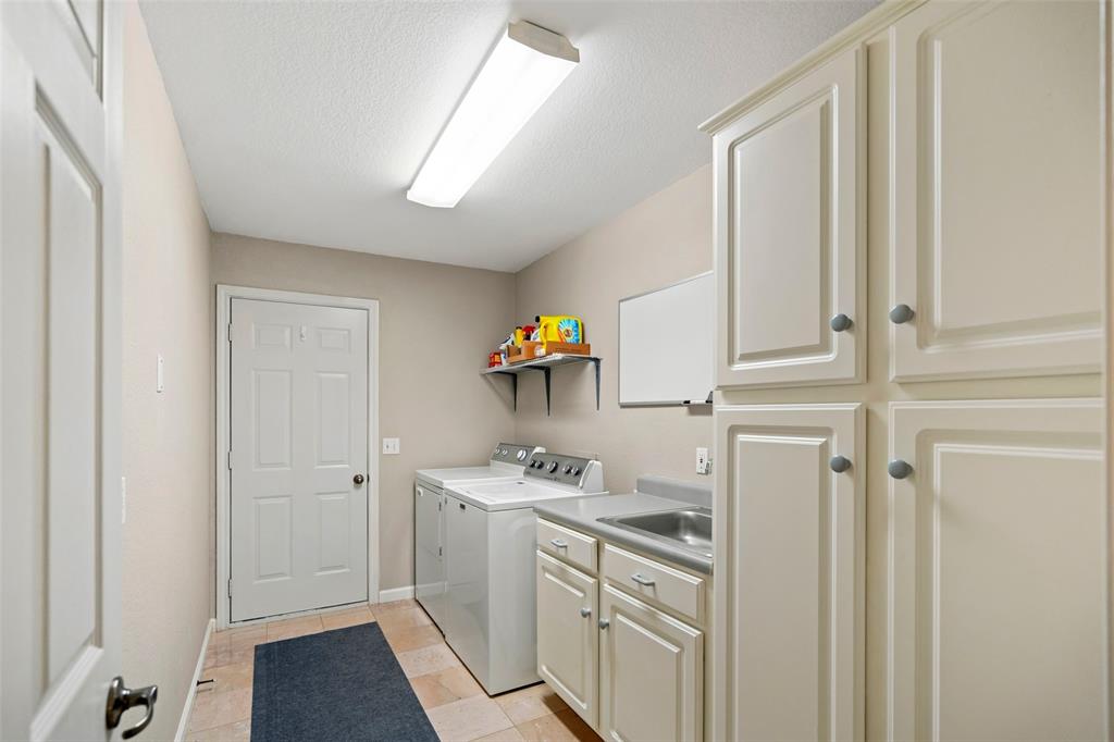 Utility area featuring shaker-style cabinetry-pantry, an integrated stainless steel sink with solid-surface countertop, tile flooring, and wall-mounted shelving