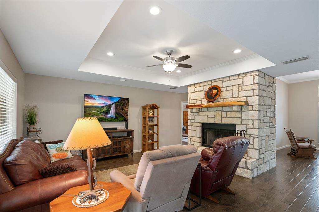 Tray ceiling featuring recessed lighting, expansive stone-clad fireplace, natural wood mantel, and dark wood-finish flooring
