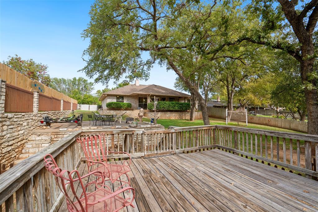 Multi-level wood decking featuring a railed perimeter, stone retaining wall, and mature shade trees
