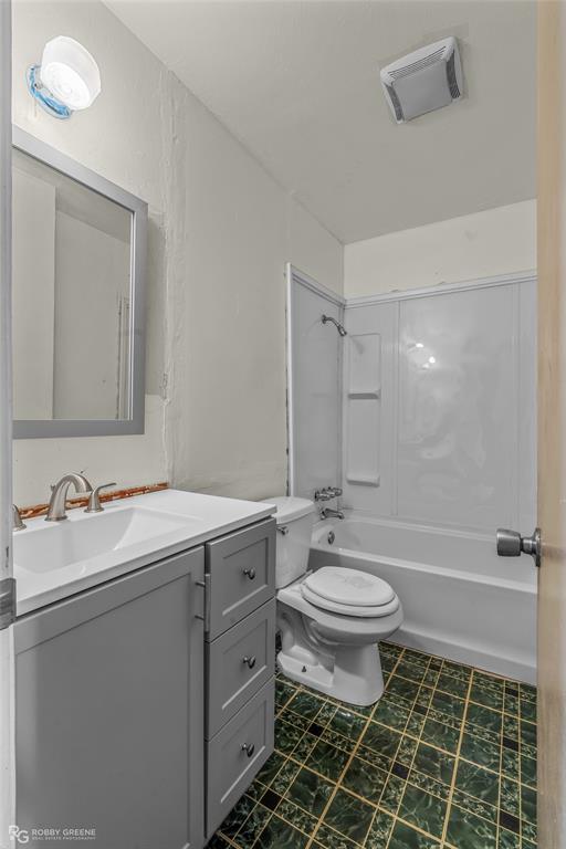 Bathroom featuring a gray vanity with a white countertop, integrated sink, wall-mounted mirror, white tub-and-shower combination, and tiled flooring