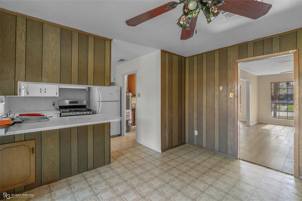 Kitchen featuring wood-paneled wall treatments, a peninsula with a solid-surface countertop, and an attached multi-blade ceiling fan with decorative glass lighting