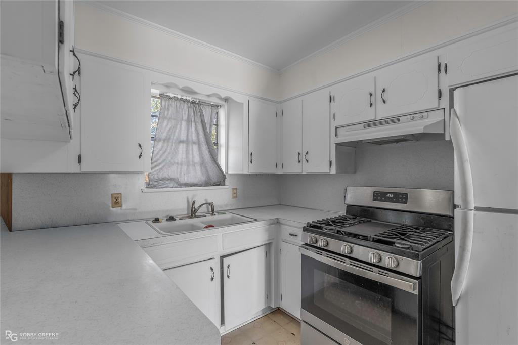 Kitchen featuring white cabinetry, solid-surface countertops, dual-basin sink, and stainless steel gas range with overhead vent hood