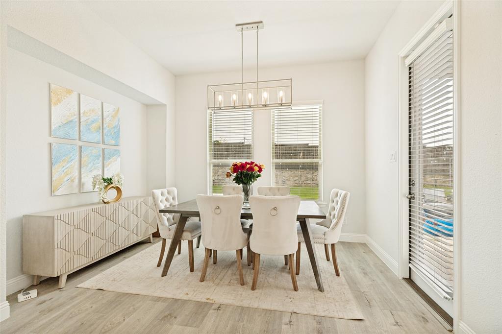 Dining area featuring wood-finish flooring, a rectangular linear pendant light fixture, dual windows, and an exterior door with integrated blinds