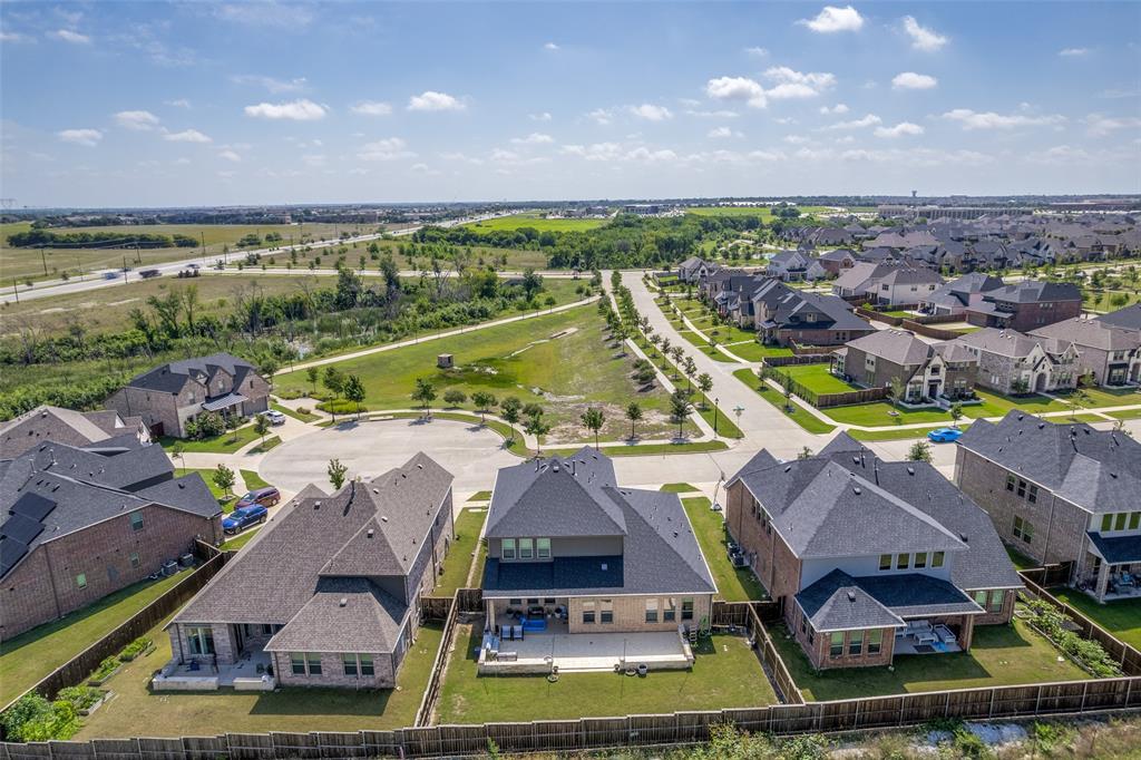 Aerial view of suburban property featuring a brick and masonry exterior, asphalt shingle roof, rear concrete patio, and fenced backyard