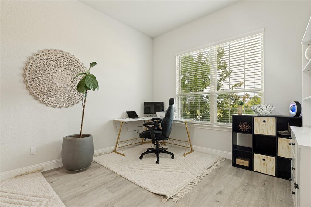 Neutral-toned room featuring wood-finish flooring, a large multi-pane window with adjustable horizontal blinds, and built-in shelving