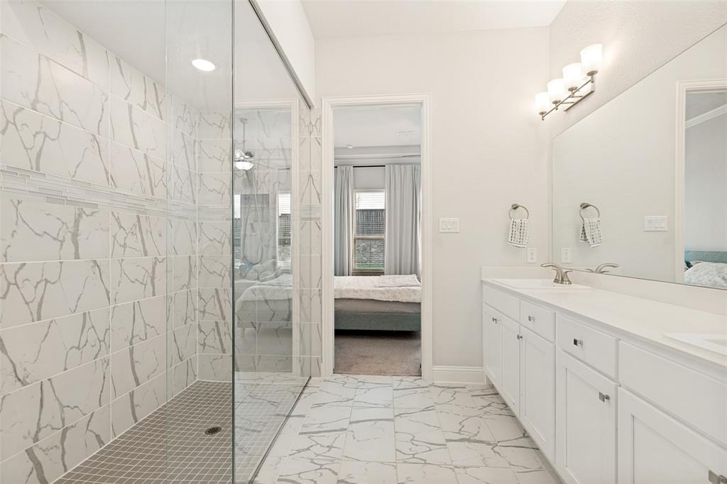 Bathroom featuring dual-sink vanity with white cabinetry, glass-enclosed walk-in shower with patterned tile surround, and tile flooring