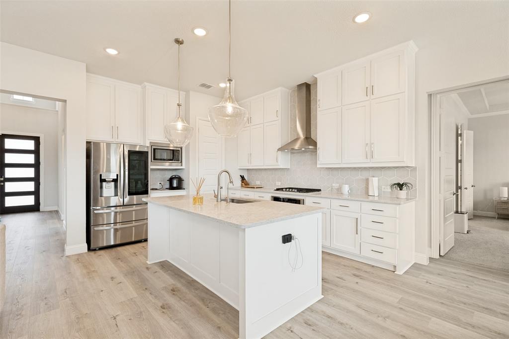 Kitchen featuring white cabinetry, an oversized central island with stone-finish countertops, stainless steel appliances, a modern chimney-style range hood, and wood-finish flooring