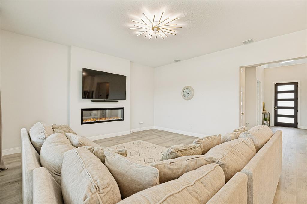 Linear recessed fireplace with stone surround, wood-finish flooring, starburst ceiling light fixture, and multipane front entry door