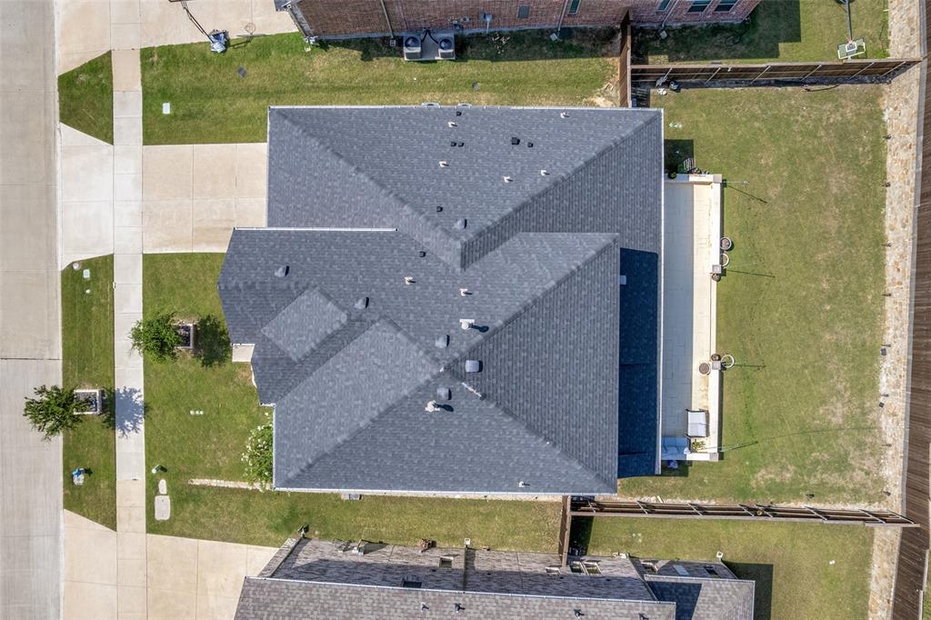 Aerial perspective showcasing a property with a multi-gabled shingled roof, a paved patio, and a fenced yard