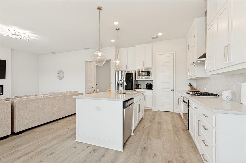 Kitchen featuring white shaker-style cabinetry, quartz countertops, a central island with a built-in stainless steel dishwasher, wood-finish flooring, and glass pendant lighting