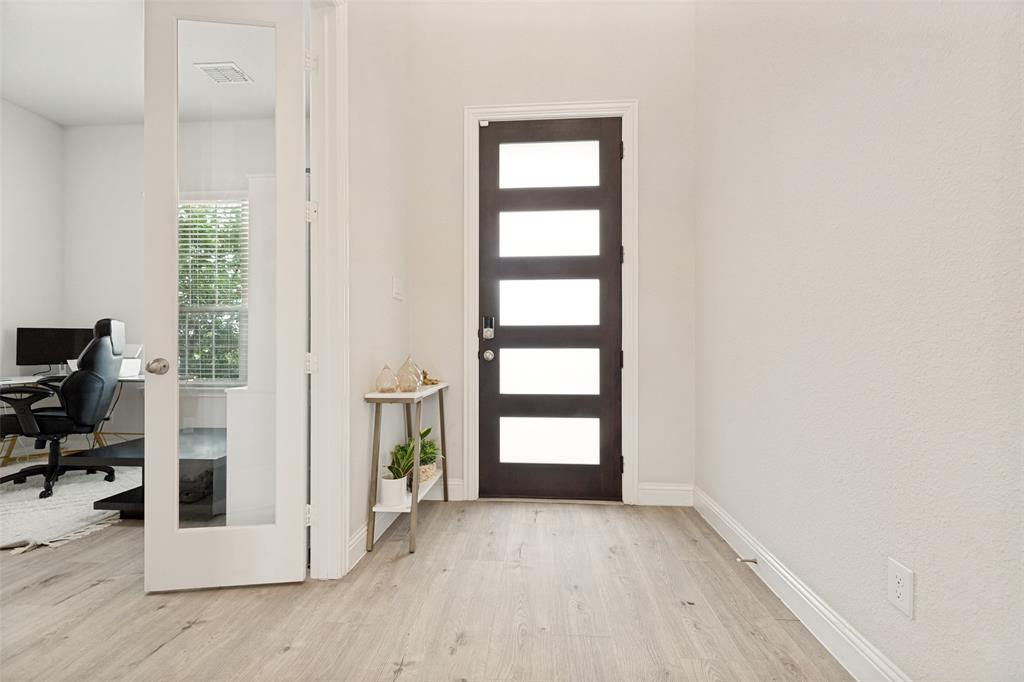 Entryway featuring wood-finish flooring, a contemporary dark-toned front door with five horizontal glass panels, and a swinging door with a full-length glass pane