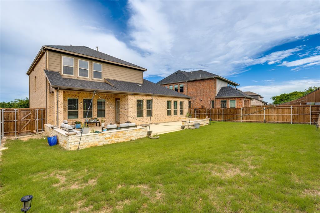 Two-story residence featuring a brick and siding exterior, expansive backyard with wood privacy fencing, and a raised stone-walled patio