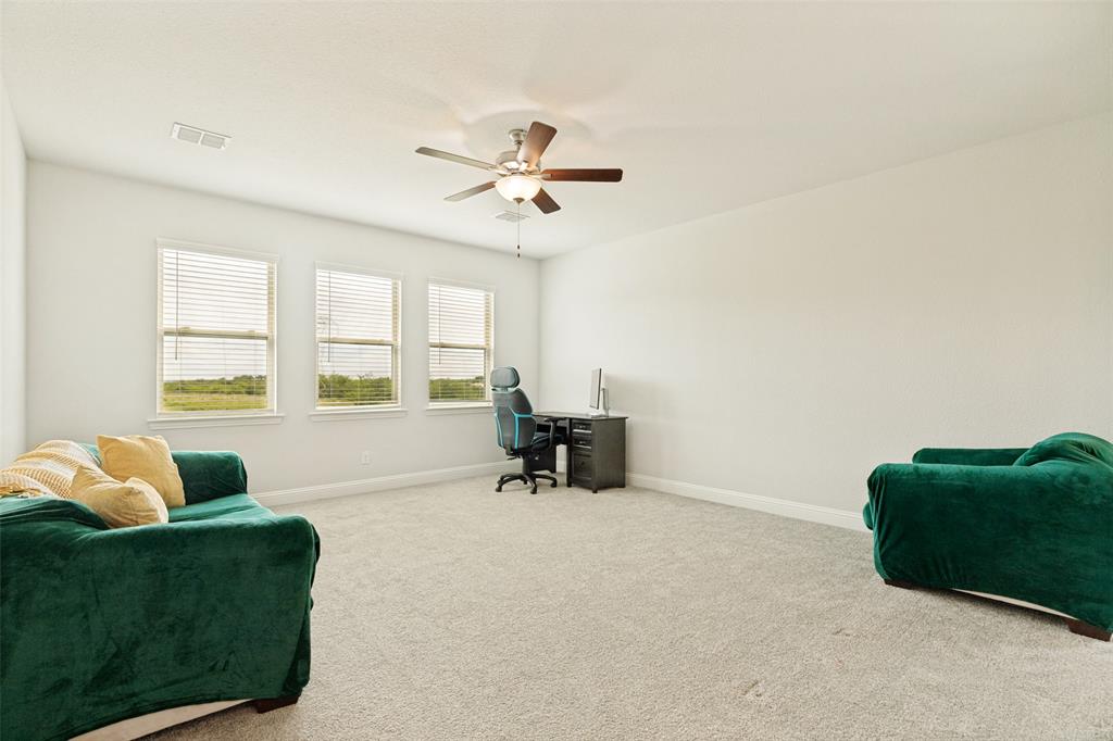 Neutral-toned carpeting, triple-window configuration with horizontal blinds, and a central ceiling fan with integrated lighting