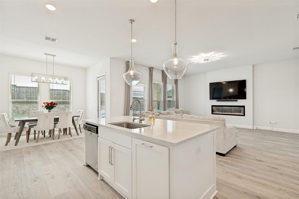 Kitchen island featuring a stone countertop, under-mount sink, and integrated dishwasher, wood-finish flooring, linear electric fireplace, and multi-pendant lighting