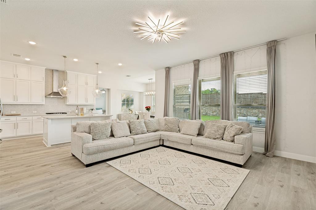 Open-concept kitchen featuring white cabinetry, a center island, and stainless steel appliances, complemented by wood-finish flooring and a multi-point sputnik-style chandelier