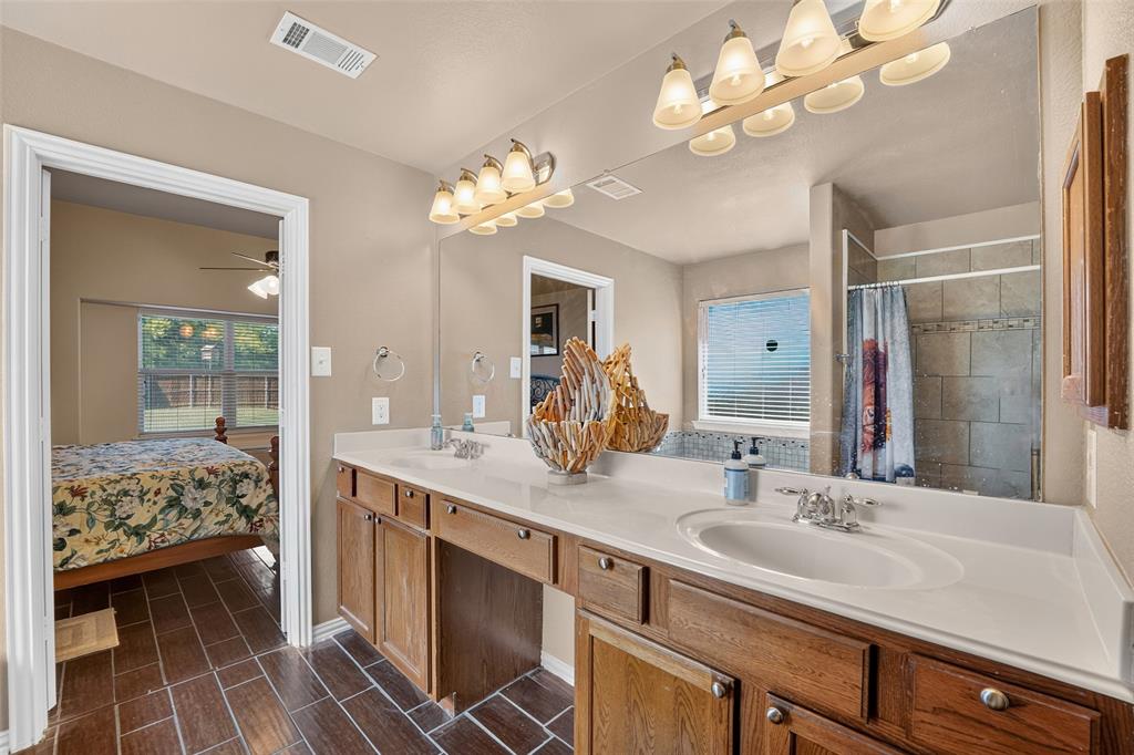 Dual-sink vanity with full-width vanity mirror, multi-light fixtures, and tiled shower and bath surround.