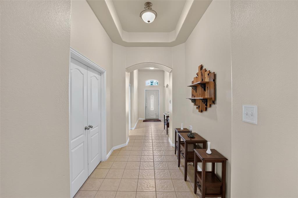 Welcome In.  There are lots of surprises and upgrades.  Let's start with this beautiful Grand Entryway featuring a tray ceiling, arched architectural opening, neutral tile flooring, and a glass-inset exterior door.  The double doors are to the bonus room/study.