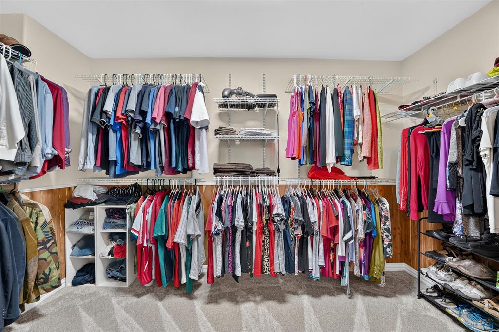 Spacious walk-in closet with cedar paneled lower walls featuring multi-level wire shelving, double hanging rods, ample storage space, and neutral carpeting.