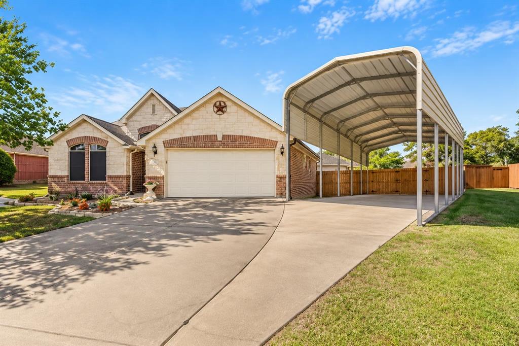 Exterior featuring a light-toned stone and brick façade, attached two-car garage, expansive concrete driveway, and a detached metal-frame carport Exterior featuring a light-toned stone and brick façade, attached two-car garage, expansive concrete driveway, and a detached metal-frame carport