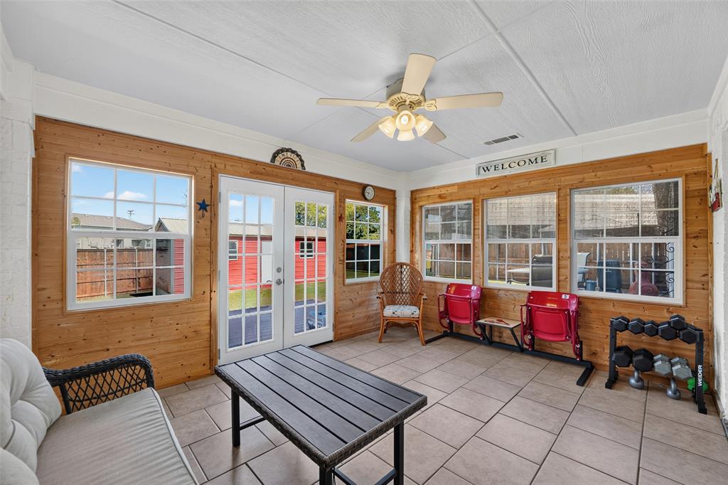 Temperature-controlled sunroom featuring abundant natural light, wood-plank walls, tile flooring, ceiling fan, and French doors leading to the backyard.