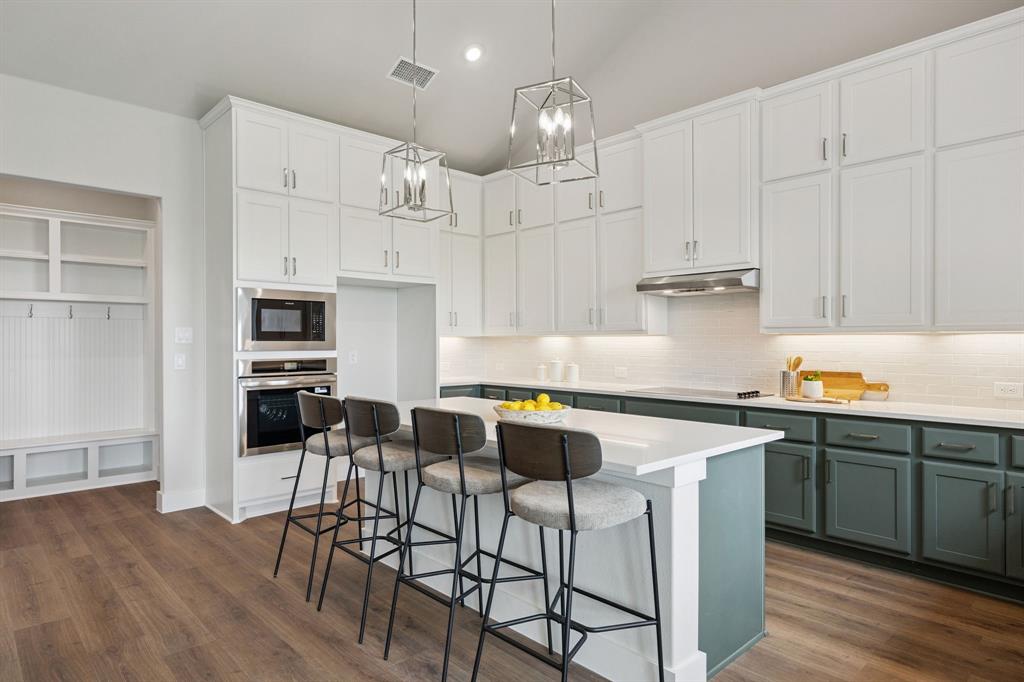 Kitchen featuring floor-to-ceiling white cabinetry, dual-tone island base, quartz countertops, built-in wall oven and microwave, and geometric pendant lighting