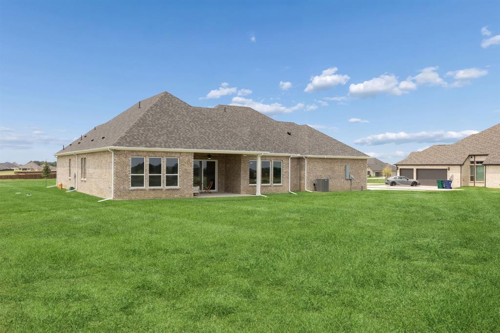 Brick exterior residence featuring an expansive lawn, a covered rear patio, and a multi-car garage