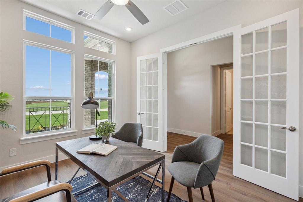 Room featuring wood-finish flooring, white French doors, tall windows with transoms, and a ceiling fan