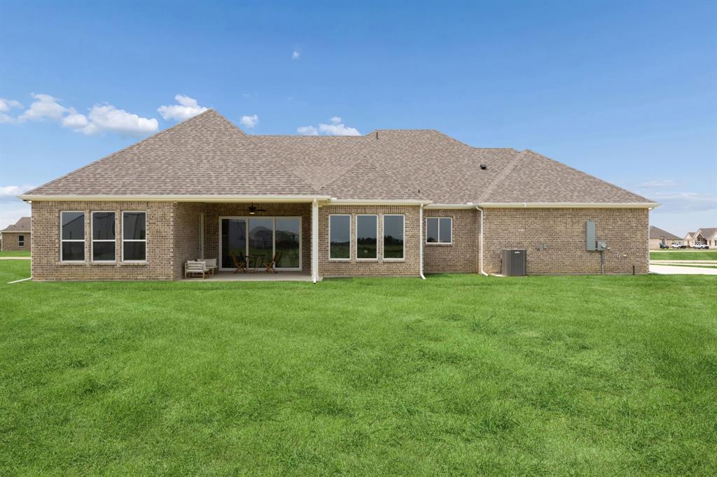 Brick exterior featuring a covered patio, shingle roof, expansive lawn, and sliding glass doors