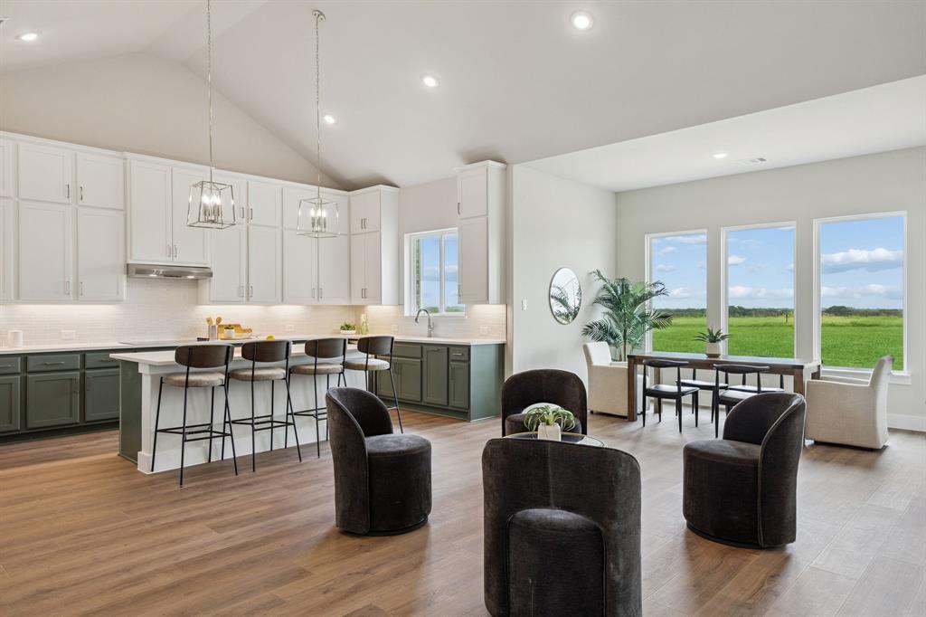 Kitchen featuring vaulted ceilings, two-tone cabinetry, a central island with counter seating, wood-finish flooring, and expansive windows