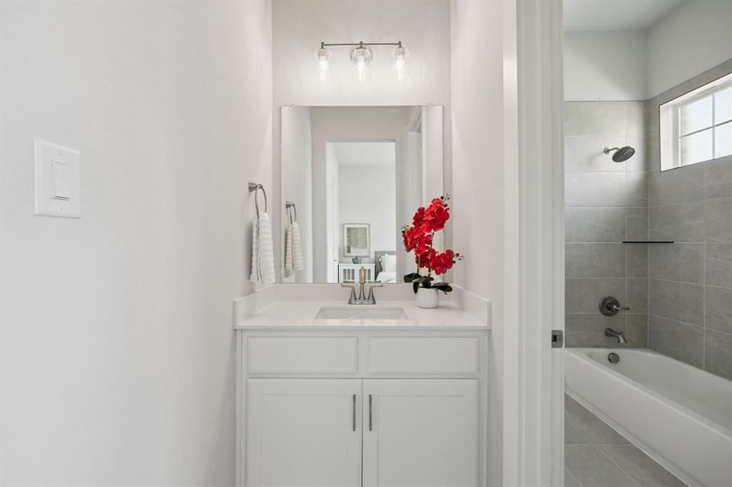Bathroom featuring white shaker-style cabinetry, a rectangular vanity sink with a polished chrome faucet, a frameless vanity mirror, a three-light fixture, and a tub-shower combination with light-toned ceramic tile surround