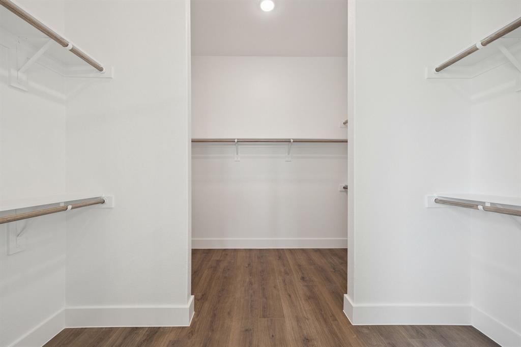 Walk-in closet featuring wood-finish flooring, white walls, and multiple tiers of built-in shelving with integrated rods