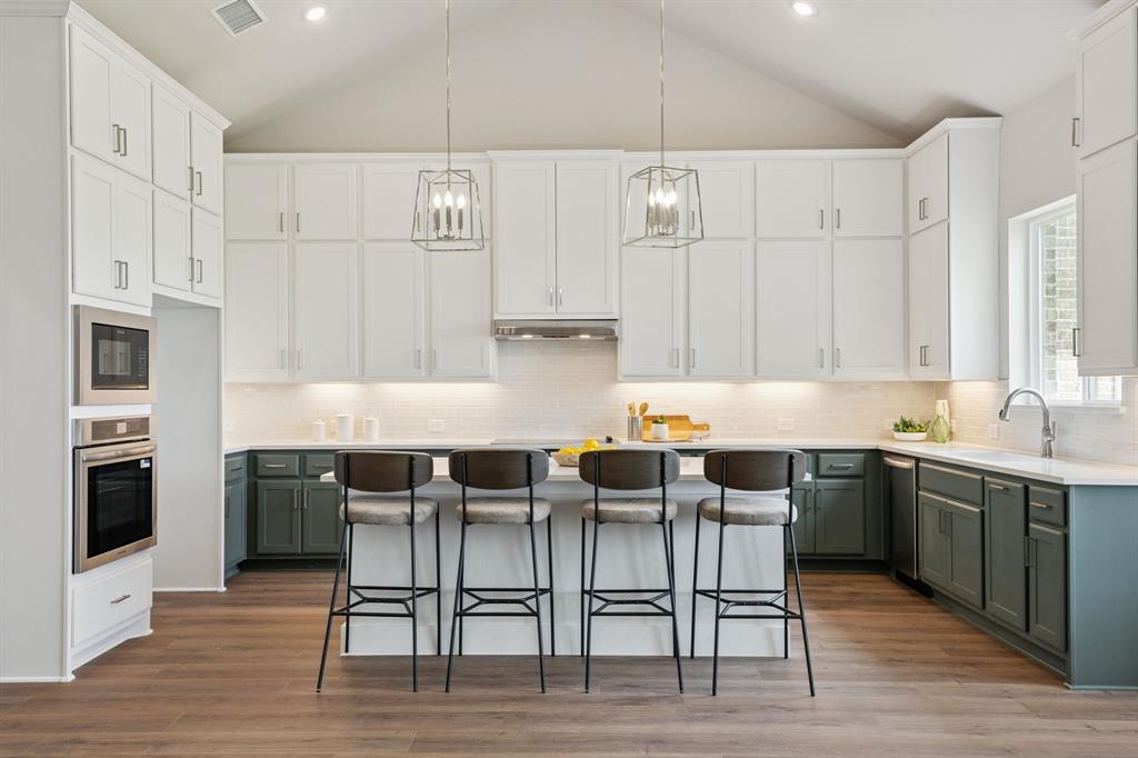 Kitchen featuring vaulted ceilings, two-tone cabinetry, a central island, integrated stainless steel double wall ovens, and wood-finish flooring