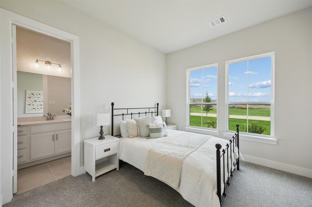 Neutral-toned bedroom featuring wall-to-wall carpeting, two oversized windows, and a bathroom equipped with a vanity featuring a light-toned countertop