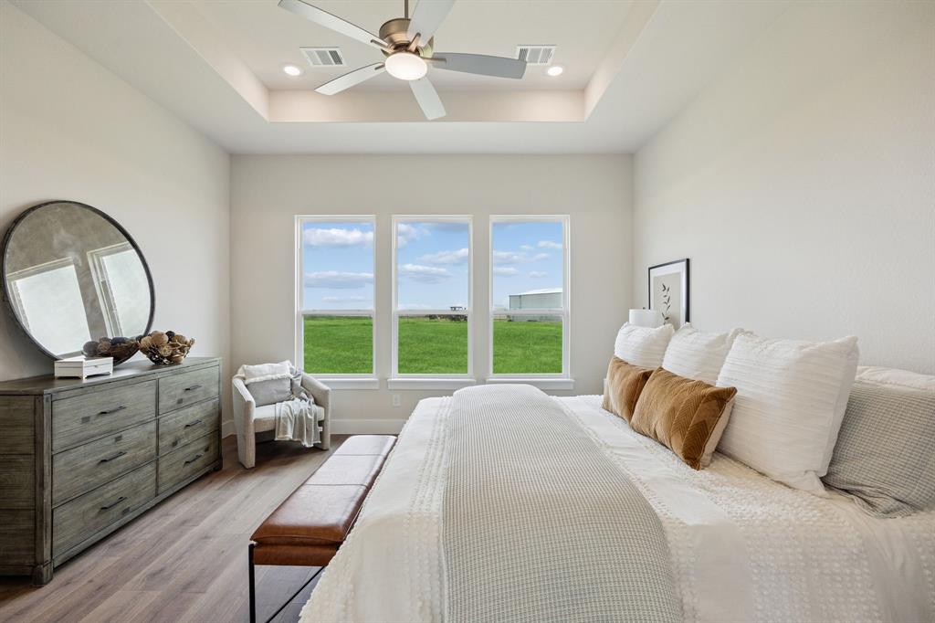 Room with a tray ceiling, wood-finish flooring, central ceiling fan, and triple windows
