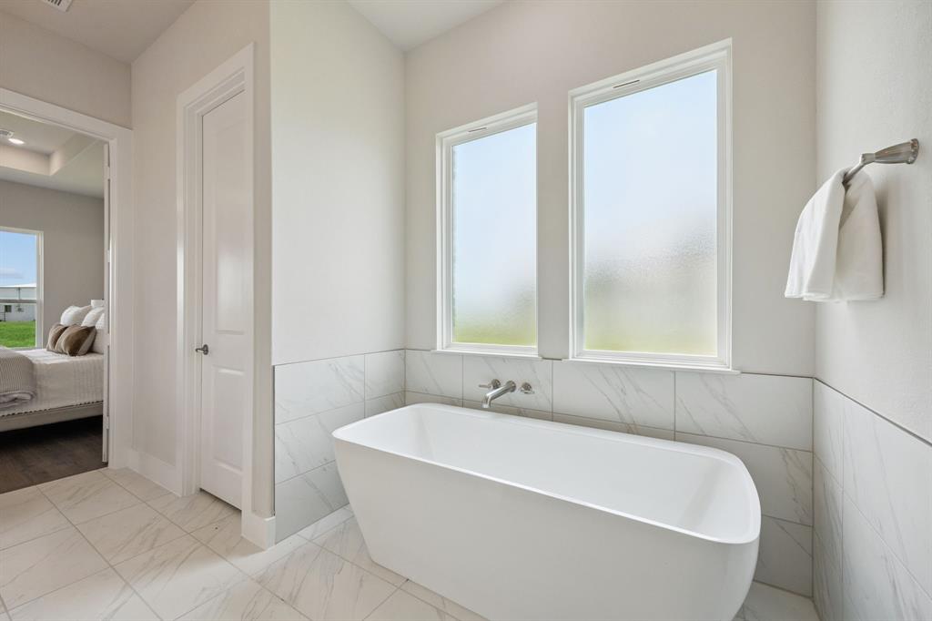 Freestanding soaking tub with a wall-mounted faucet, dual windows with frosted glass, and large-format tile surround